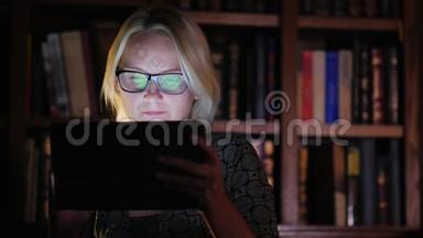 一个戴眼镜的女人在书架的背景上用平板电脑工作，上面有书。 概念图书馆、工作或学习，直至
